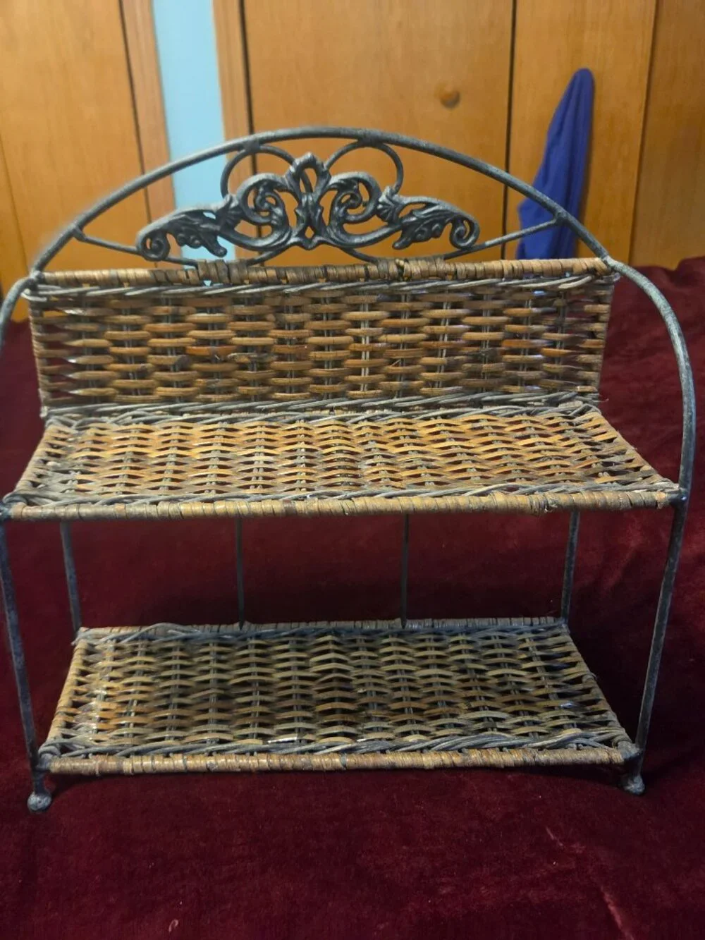 two tier wicker shelf with metal frame adorned with scrollwork some wear